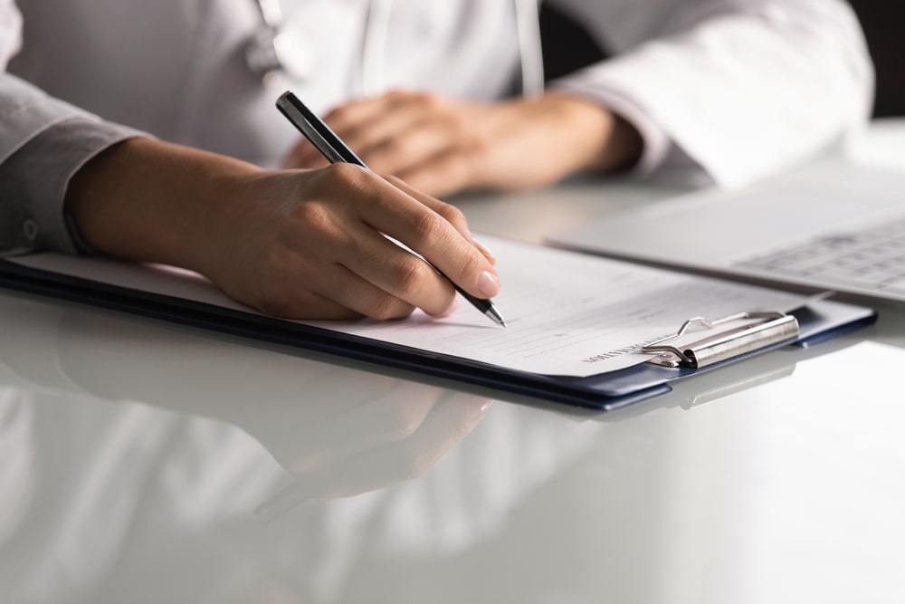 Close up professional female doctor wearing uniform taking notes in journal, physician therapist practitioner filling medical documents
