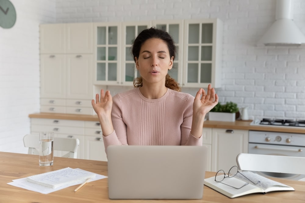Young Hispanic businesswoman sit at table in kitchen near computer closed eyes makes breathing technique calming exercises additional addiciton treament
